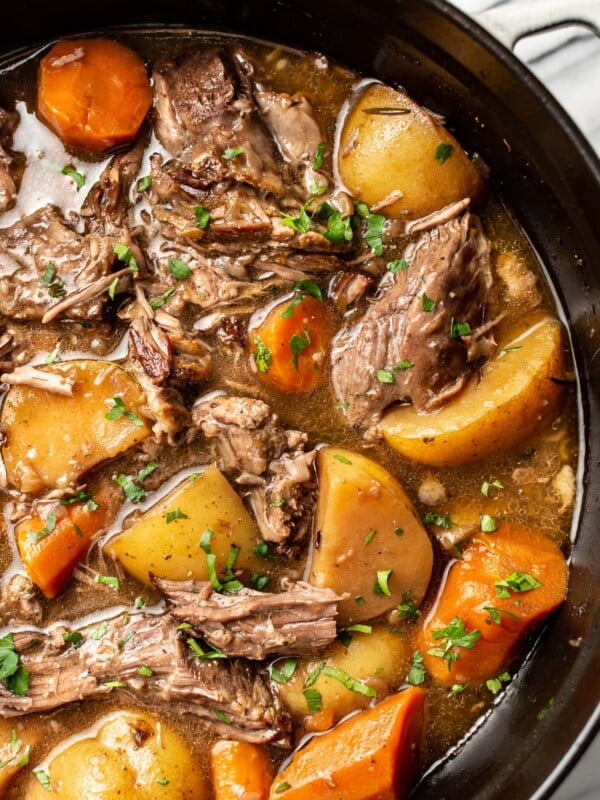 a dutch oven with pot roast beef, potatoes, and carrots