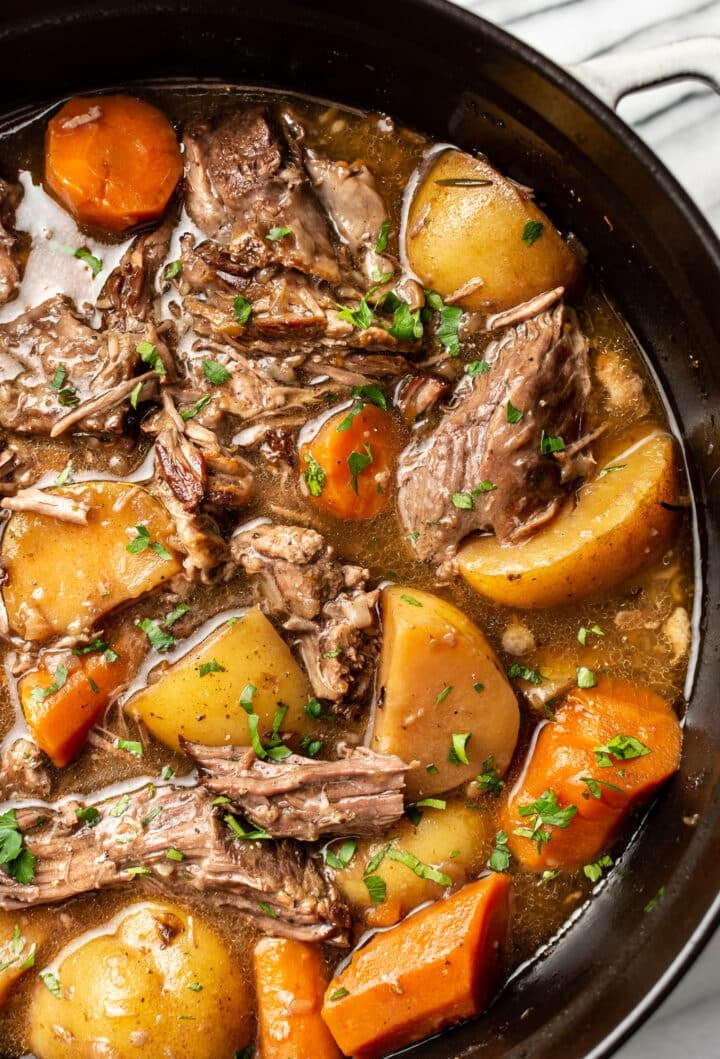 a dutch oven with pot roast beef, potatoes, and carrots