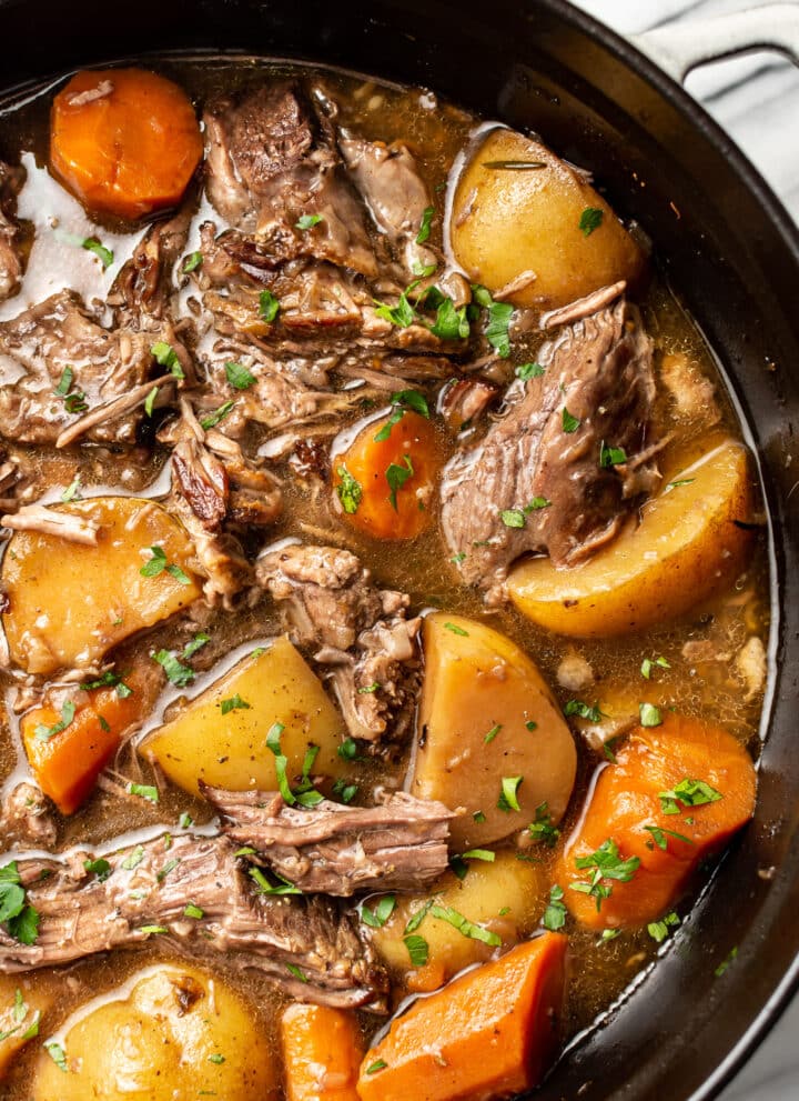 a dutch oven with pot roast beef, potatoes, and carrots