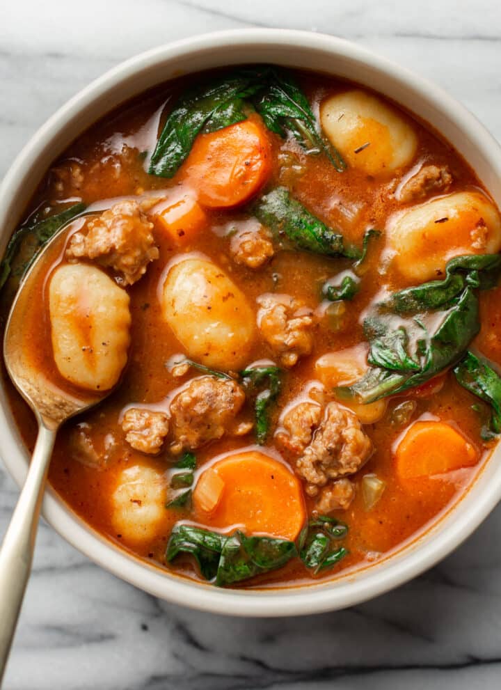 a bowl of sausage gnocchi soup with a spoon