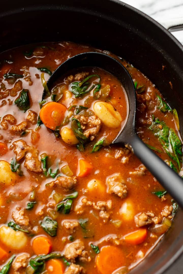 a ladle in a pot of sausage gnocchi soup