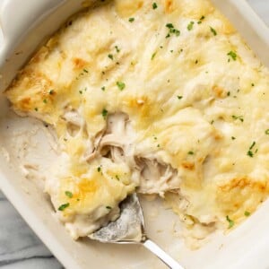 a baking dish with chicken alfredo ravioli bake and a serving spoon