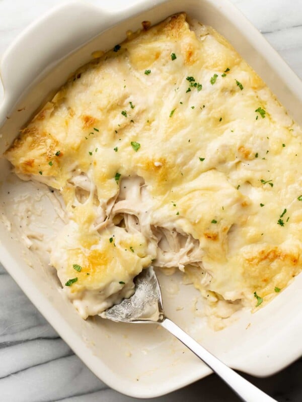 a baking dish with chicken alfredo ravioli bake and a serving spoon