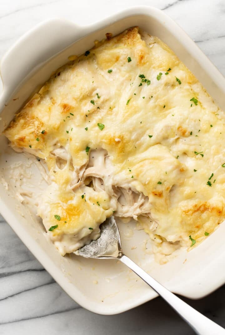 a baking dish with chicken alfredo ravioli bake and a serving spoon