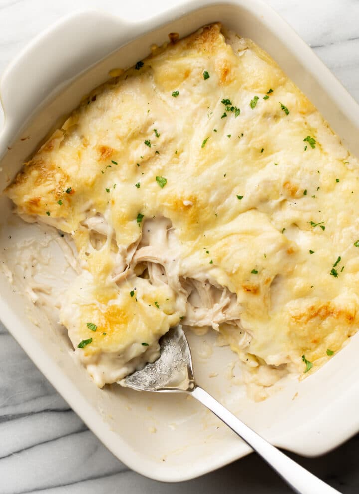 a baking dish with chicken alfredo ravioli bake and a serving spoon