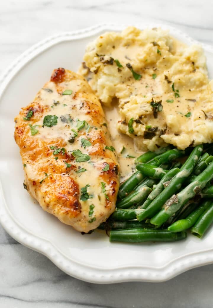 a plate with tarragon chicken, green beans, mashed potatoes, and creamy sauce