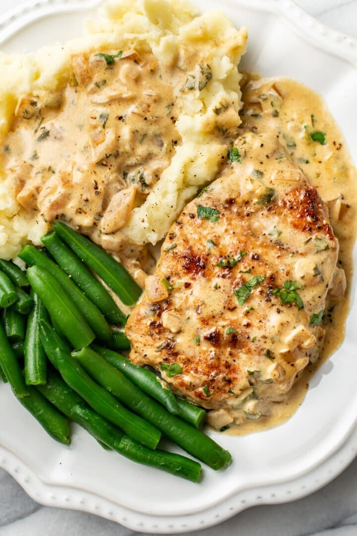 a plate with a boursin pork chop, green beans, and mashed potatoes