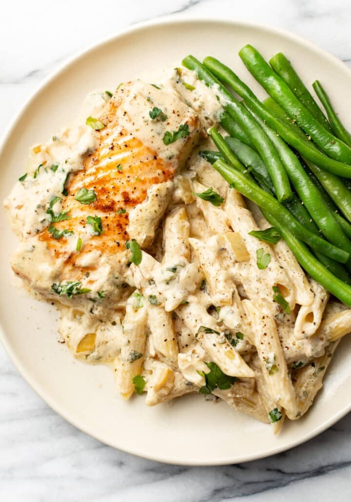 a plate with a piece of salmon, boursin sauce, penne, and green beans