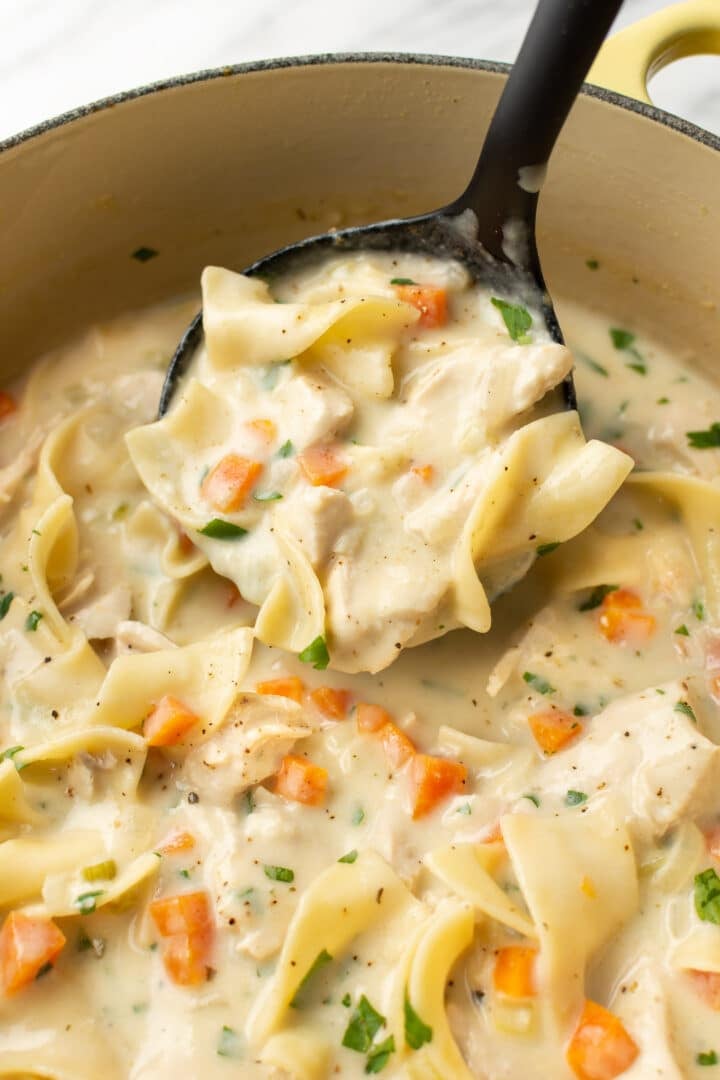 a ladle of creamy chicken noodle soup in a dutch oven