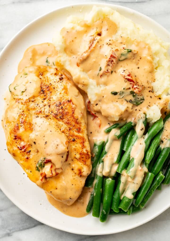 a plate of marry me chicken, mashed potatoes, and green beans