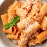 a bowl of rigatoni pasta with pink sauce, parmesan, and basil