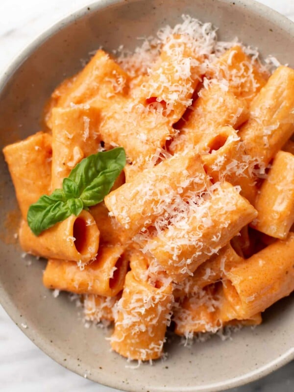 a bowl of rigatoni pasta with pink sauce, parmesan, and basil