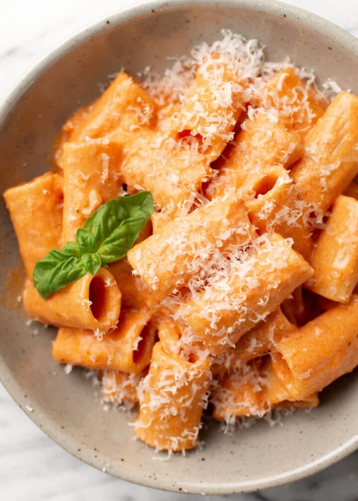 a bowl of rigatoni pasta with pink sauce, parmesan, and basil