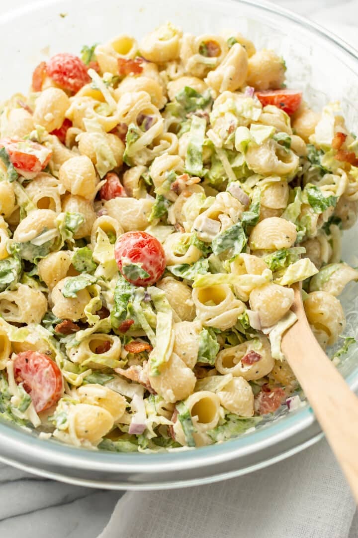 closeup of a bowl of blt pasta salad with a wooden serving spoon