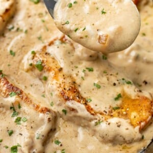 closeup of a spoonful of sauce over a skillet of cream of mushroom soup pork chops