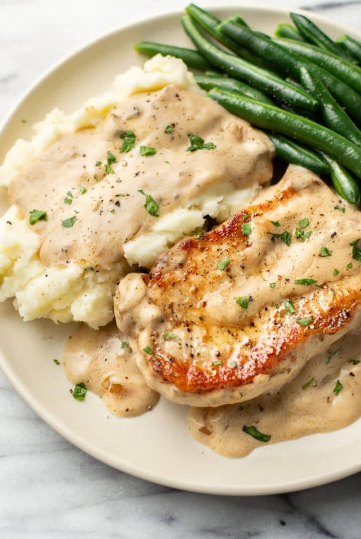 a plate with a pork chop, cream of mushroom sauce, green beans, and mashed potatoes