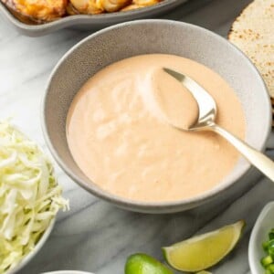 a bowl of fish taco sauce with a spoon next to taco ingredients