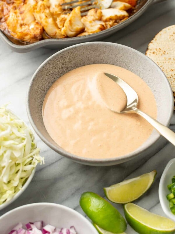 a bowl of fish taco sauce with a spoon next to taco ingredients