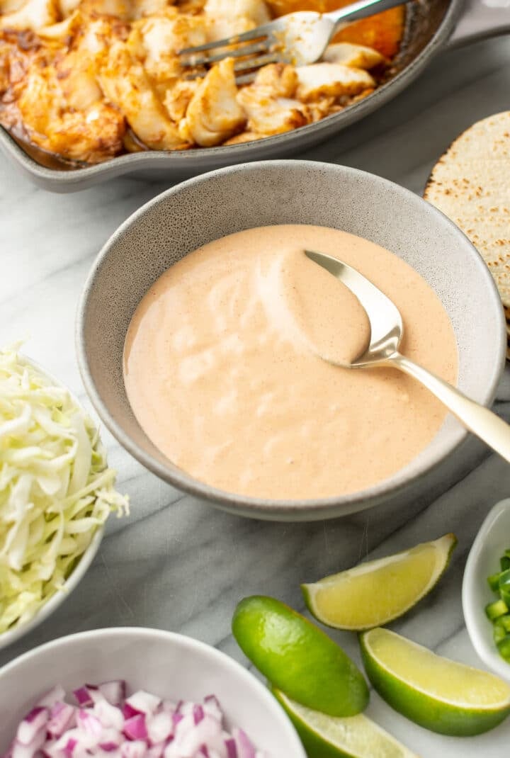 a bowl of fish taco sauce with a spoon next to taco ingredients