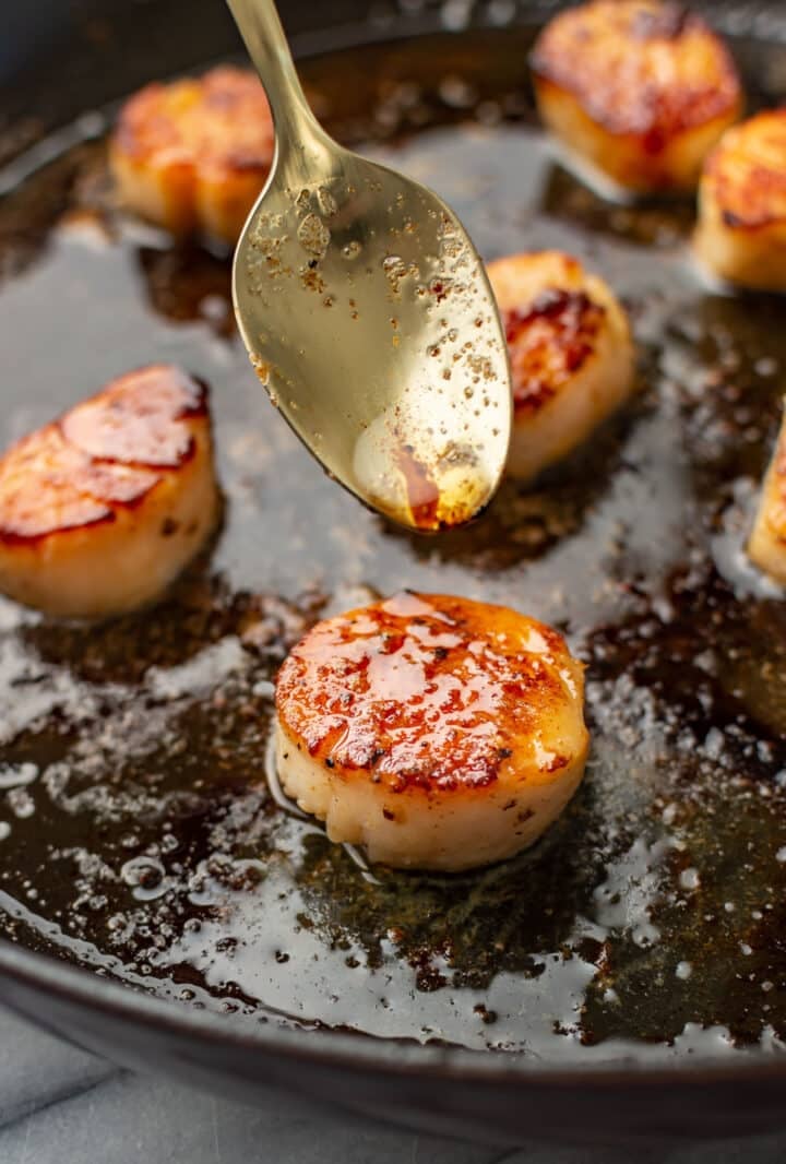 closeup of a skillet with seared scallops and a spoon