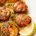 a plate with pan seared scallops next to lemon wedges