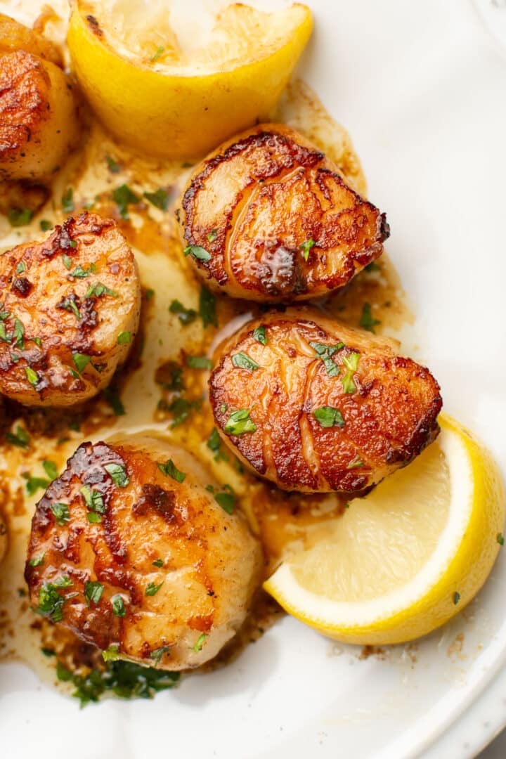 a plate with pan seared scallops next to lemon wedges