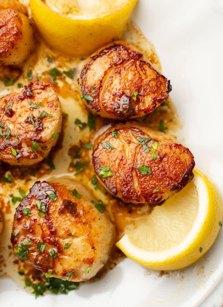 a plate with pan seared scallops next to lemon wedges