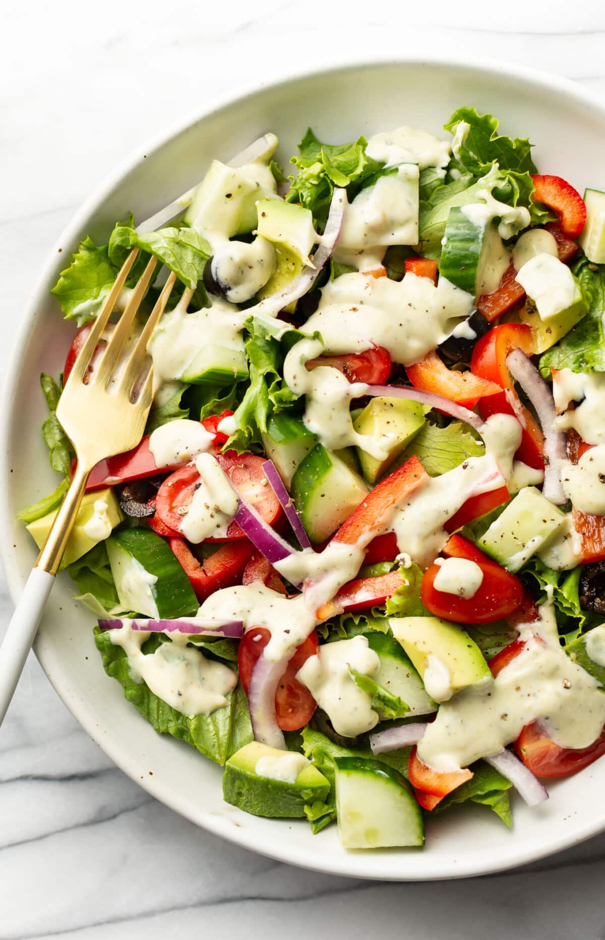 a bowl of salad with creamy pesto dressing and a fork