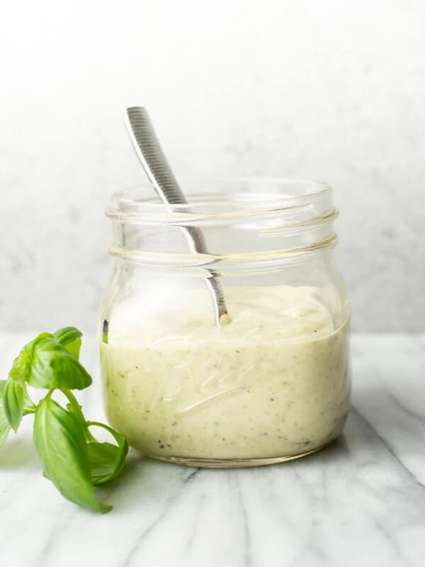 a glass jar with creamy pesto dressing, a spoon, and a sprig of basil