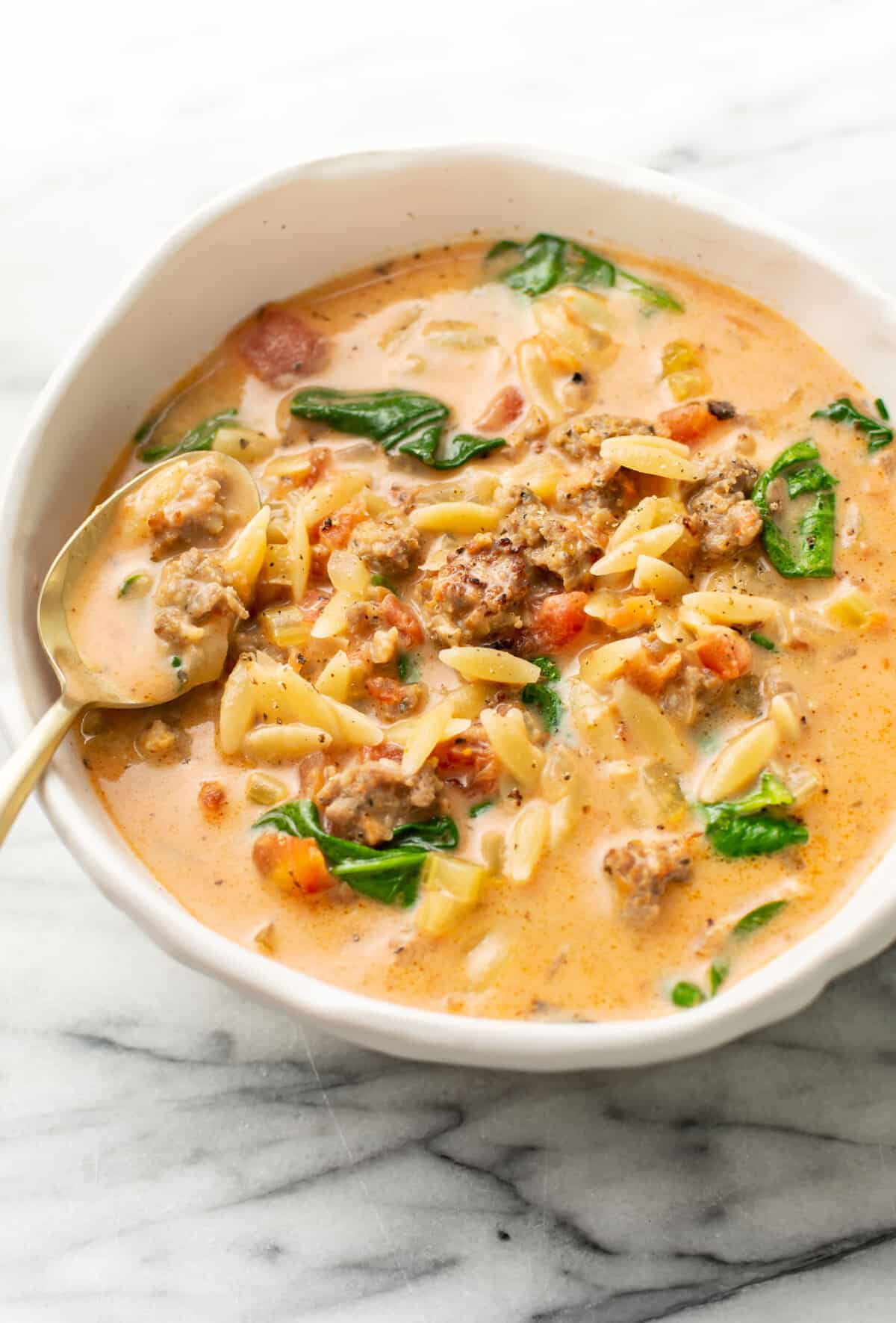 a bowl of italian sausage orzo soup with a spoon