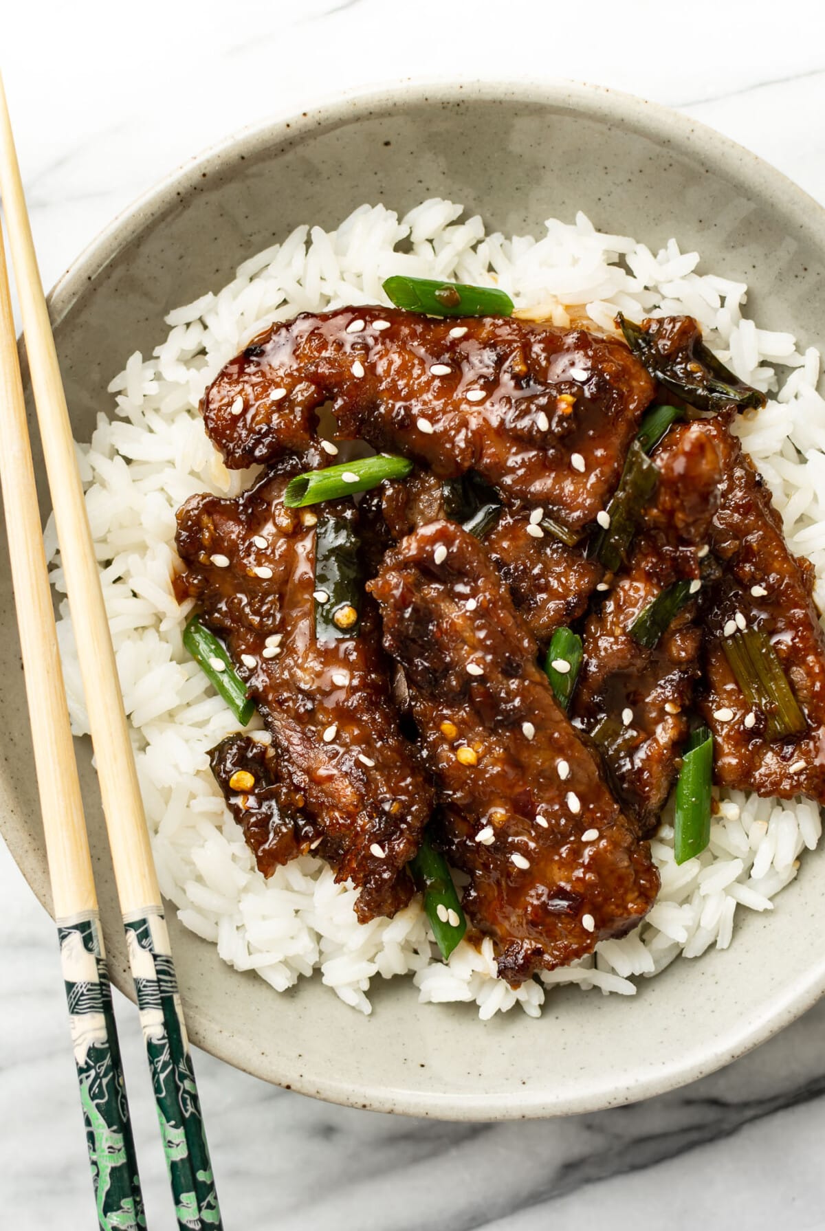 a bowl of mongolian beef over rice with chopsticks
