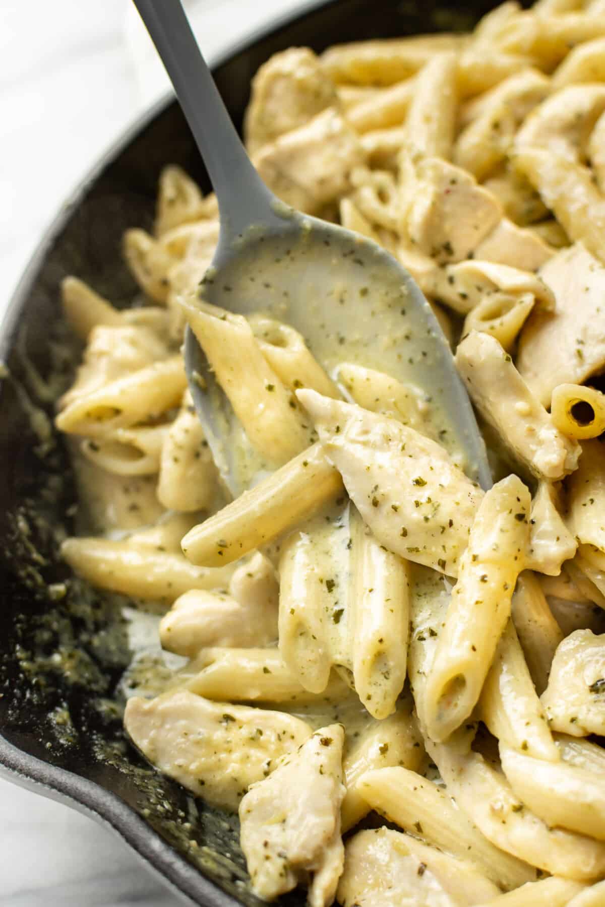 a skillet with creamy chicken pesto pasta and a serving spoon