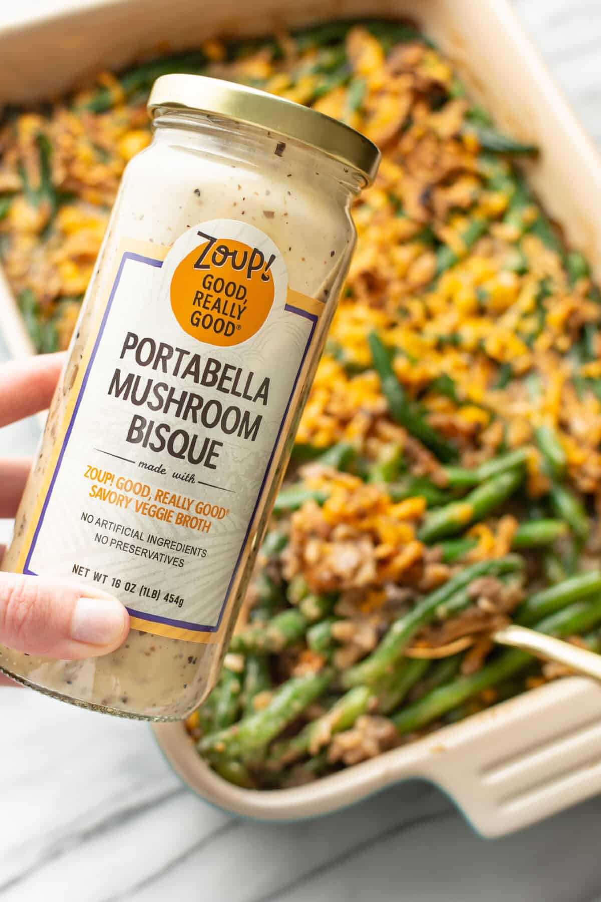 a baking dish with fresh green bean casserole and a jar of mushroom soup in the foreground