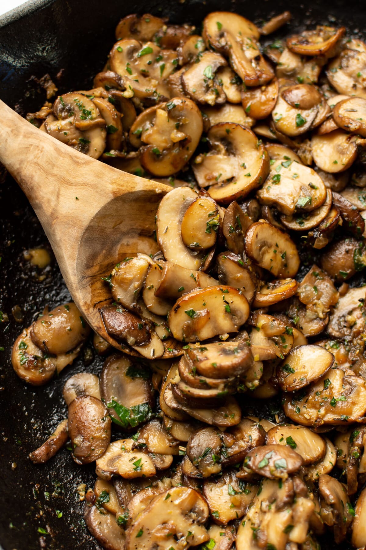 a skillet with sauteed mushrooms and a wooden spoon