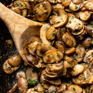 a skillet with sauteed mushrooms and a wooden spoon