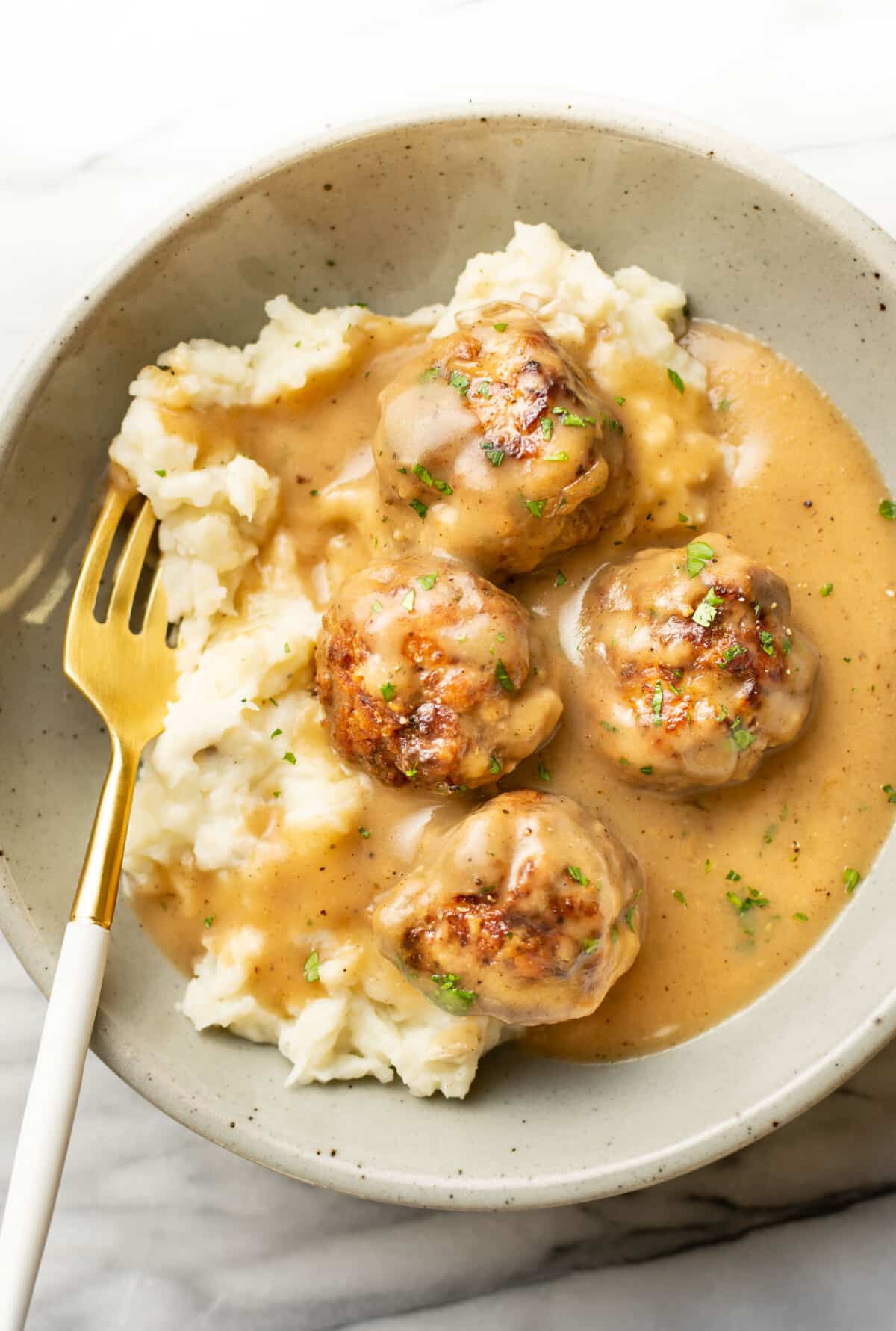 a bowl with meatballs and gravy over mashed potatoes with a fork