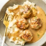 a bowl with meatballs and gravy over mashed potatoes with a fork