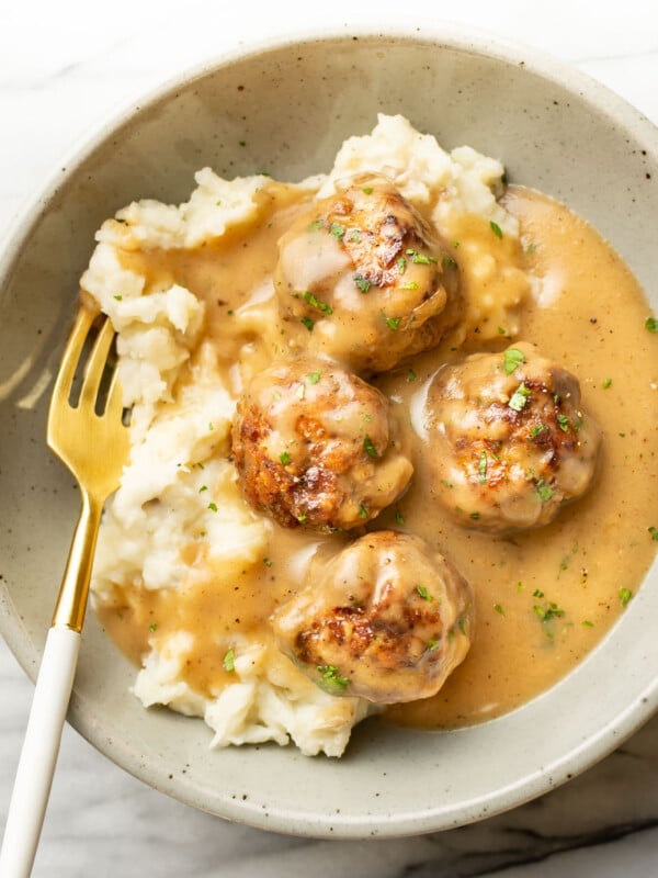 a bowl with meatballs and gravy over mashed potatoes with a fork