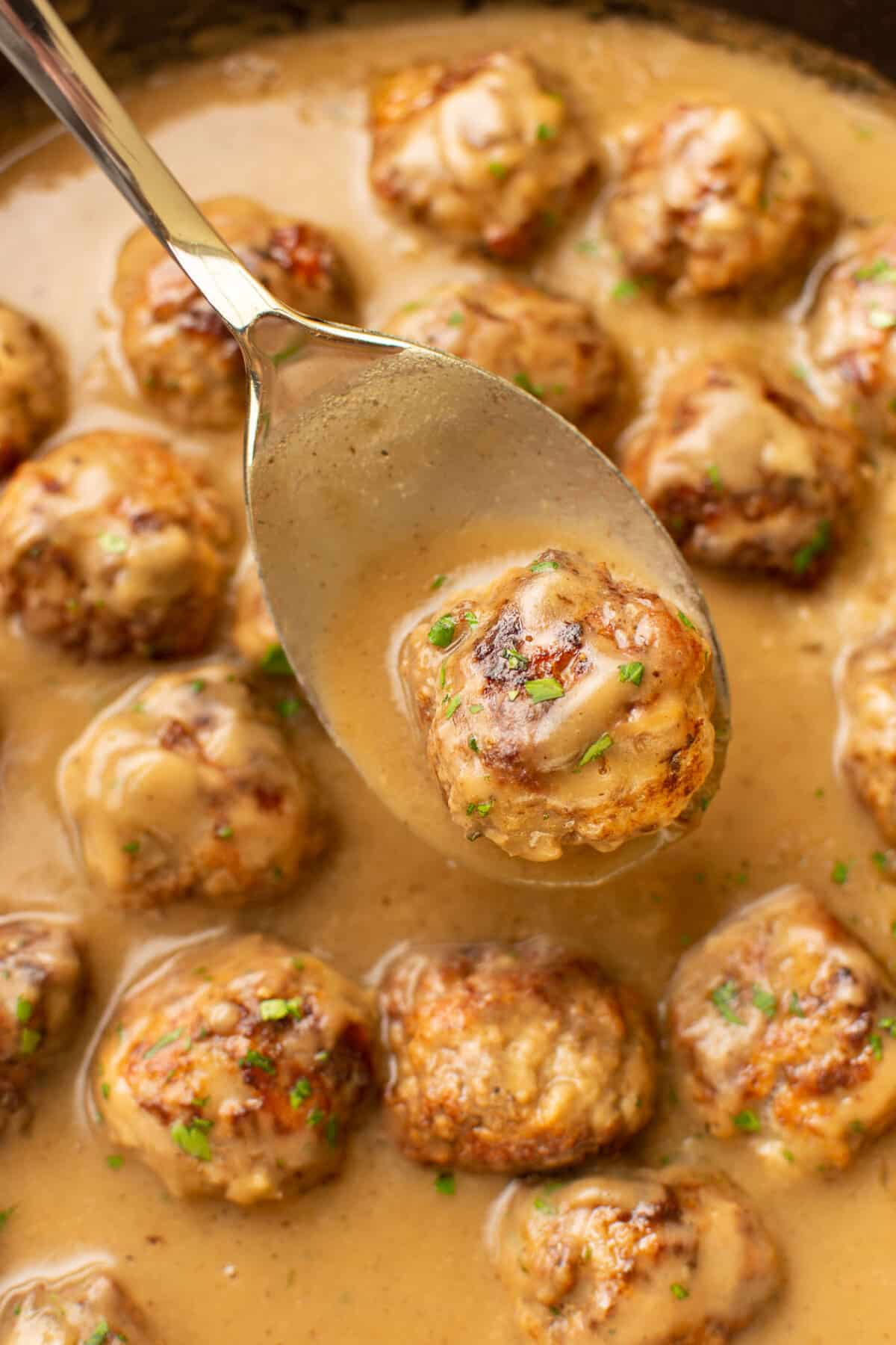 closeup of a skillet with meatballs in gravy and a serving spoon