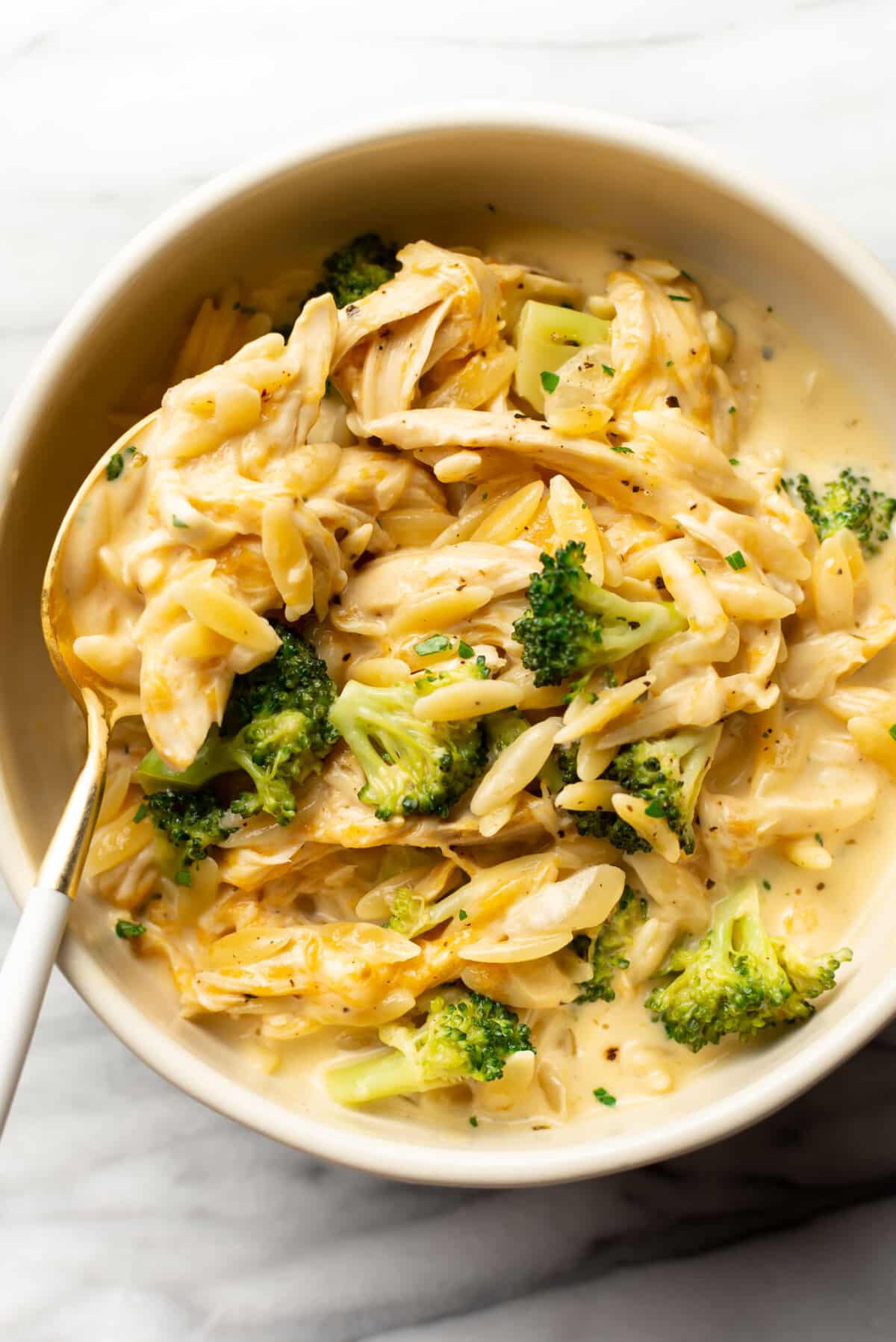 a bowl with cheesy chicken broccoli orzo and a spoon