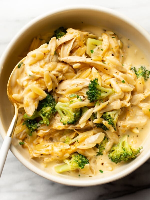 a bowl with cheesy chicken broccoli orzo and a spoon