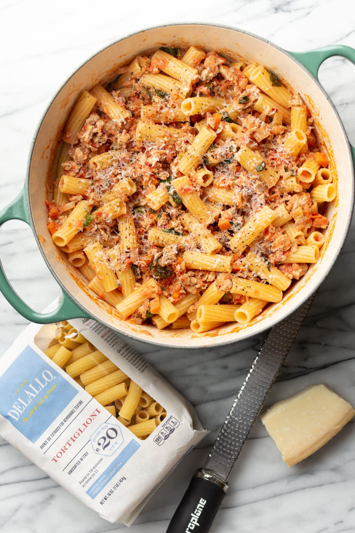 a dutch oven with ground turkey pasta next to a block of parmesan and a package of pasta