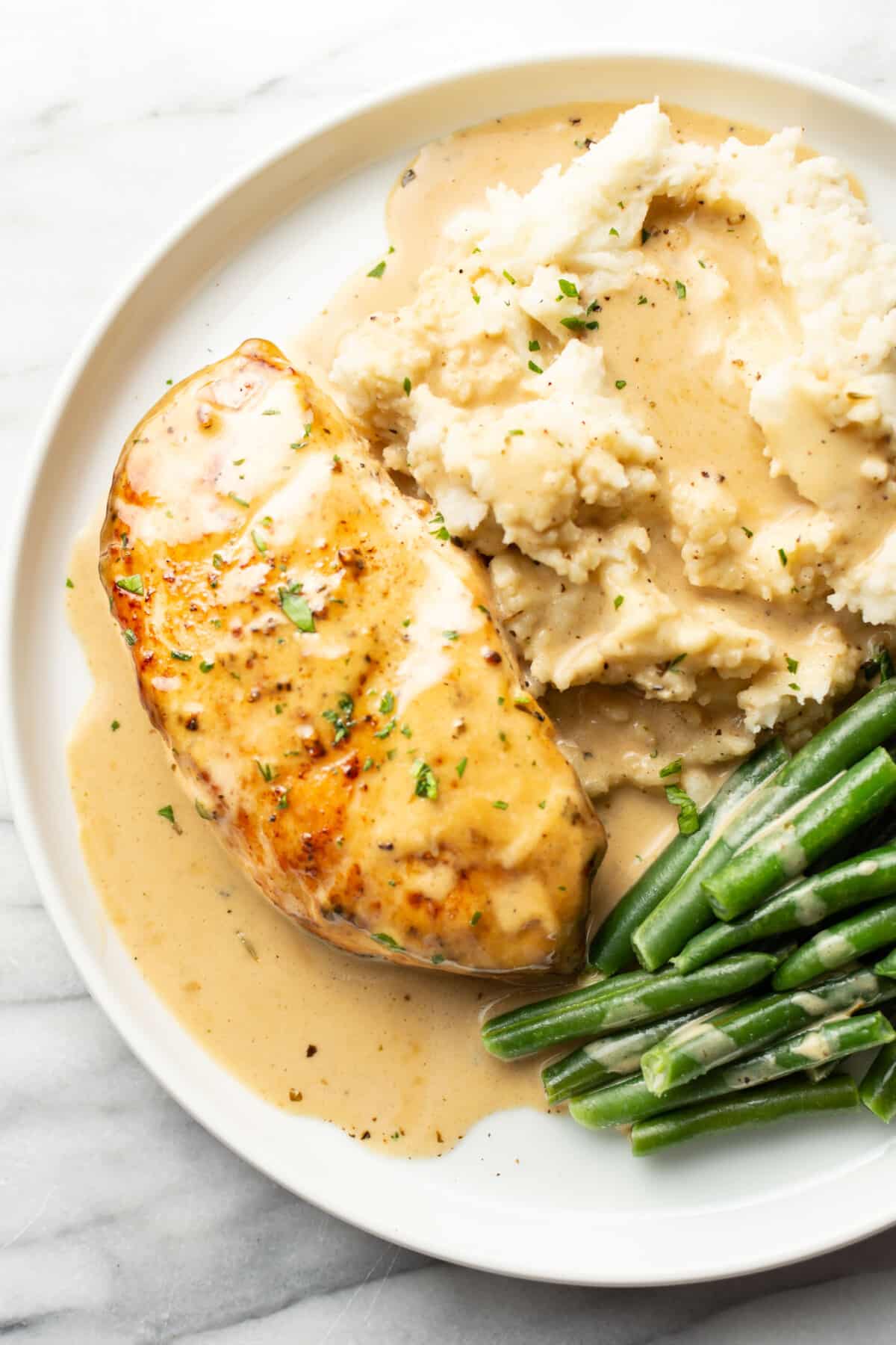 a plate with creamy maple chicken, mashed potatoes, and green beans