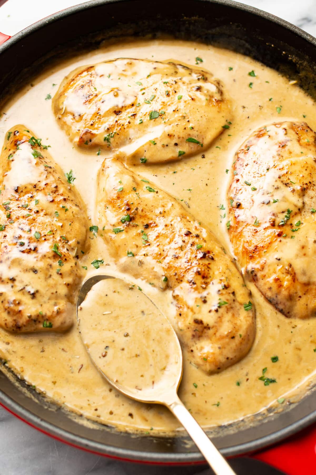 a skillet with creamy maple chicken and a serving spoon