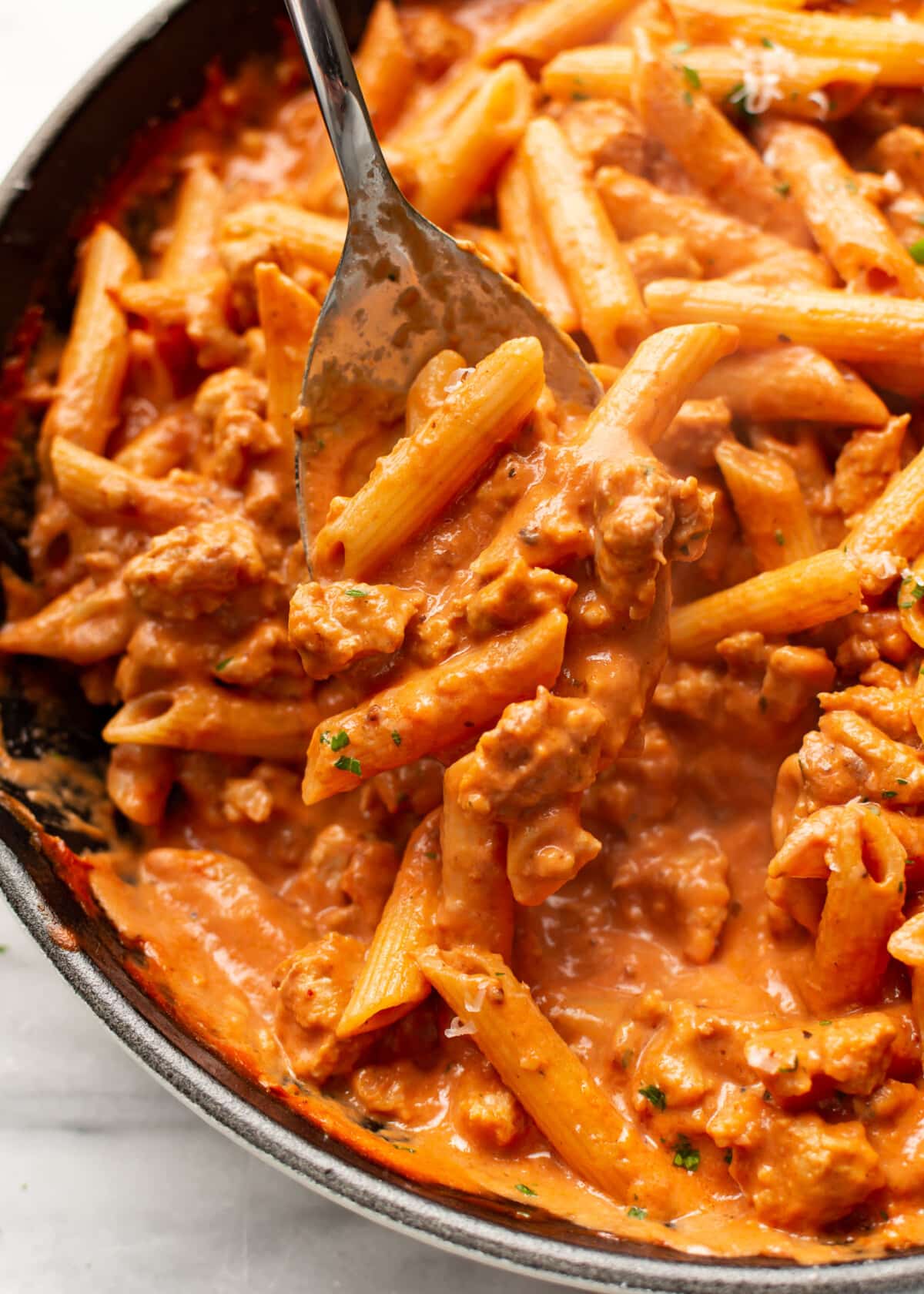 closeup of a skillet with a serving spoon and creamy sausage tomato pasta