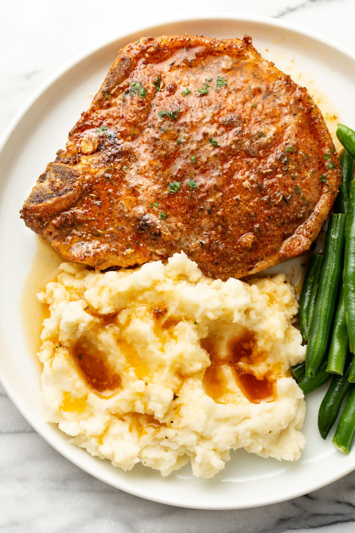 a plate with a baked pork chop, mashed potatoes, green beans, and sauce