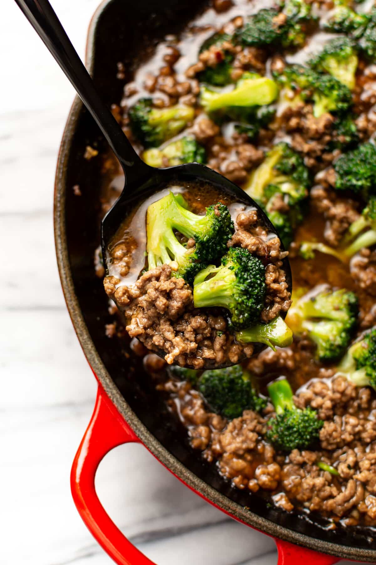 closeup of a skillet with ground beef and broccoli and a serving spoon