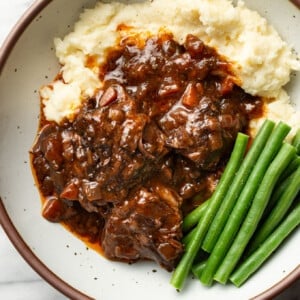 a bowl with red wine braised short ribs, mashed potatoes, and green beans