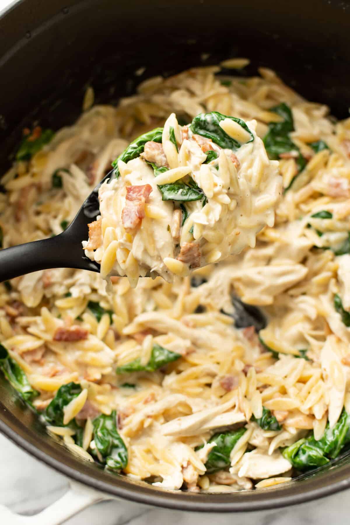 closeup of a dutch oven with chicken bacon ranch orzo and a serving spoon