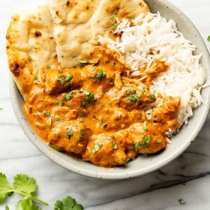 a bowl of butter chicken with basmati rice and naan